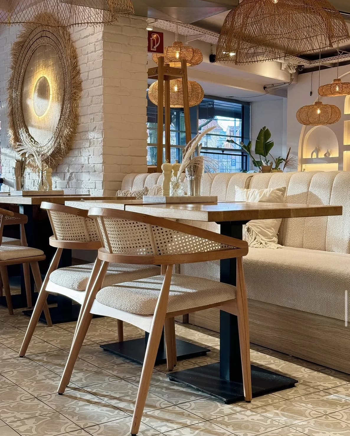 Innenraum des Café Bohoo: helle Sitzbank, Holzstühle mit Wiener Geflecht und Rattanleuchten vor weißer Backsteinwand